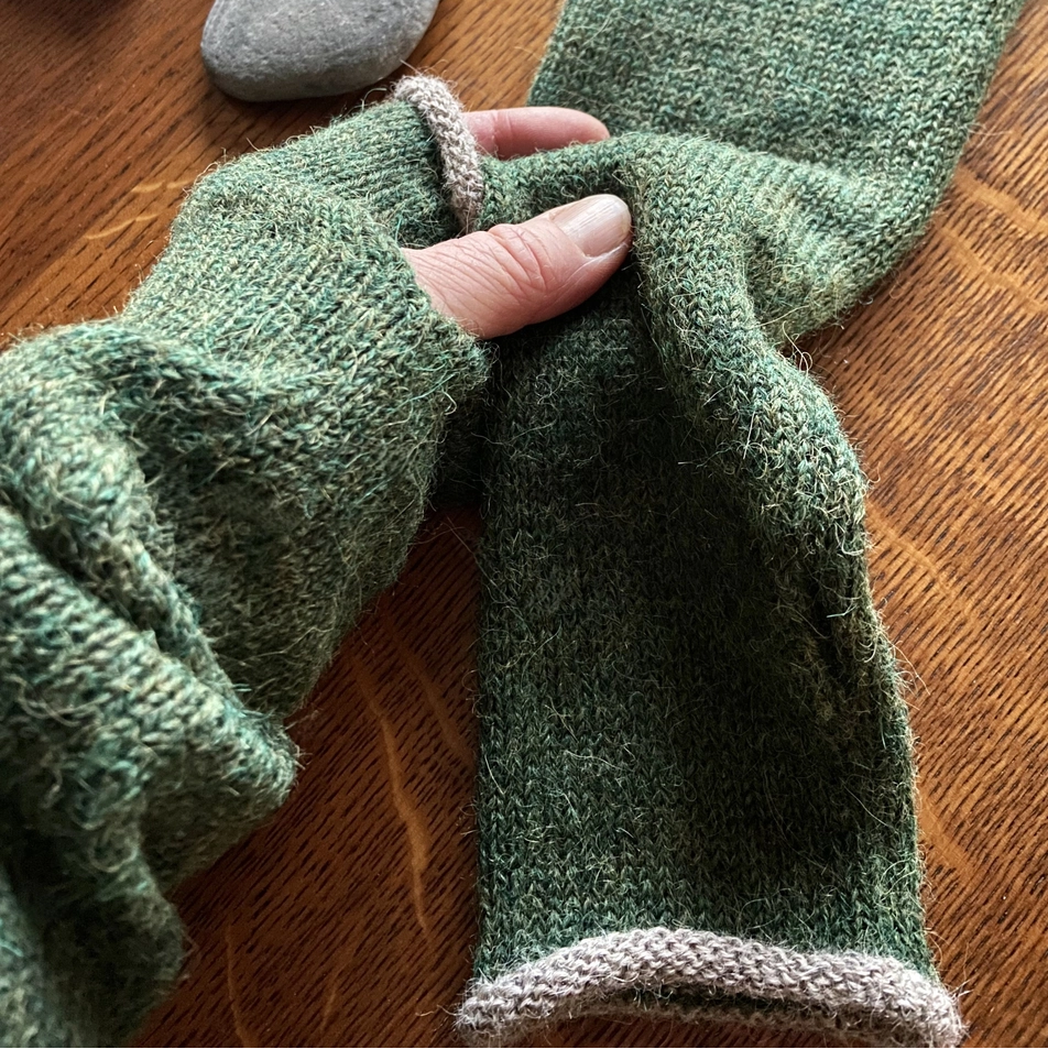 Green knitted gloves being worn on a wooden surface with a stone and in the background.