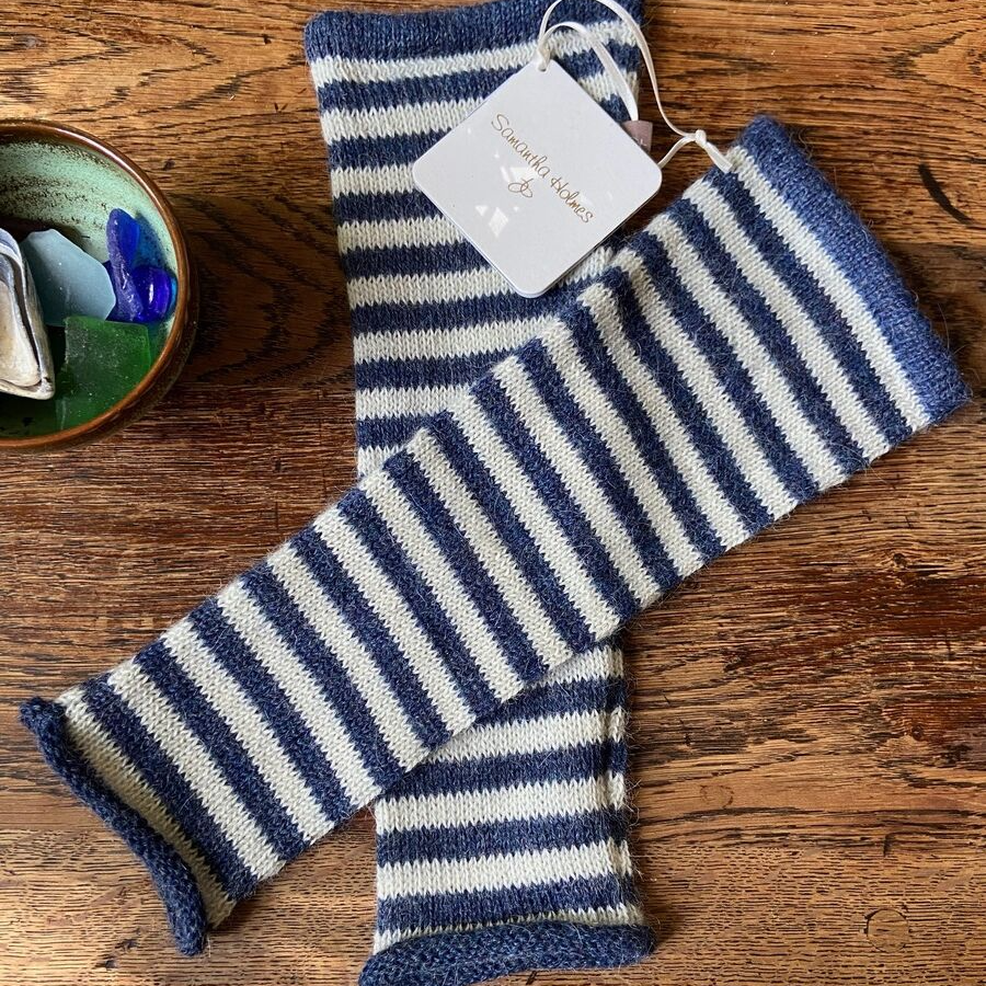 Blue and white striped wrist warmers on a wooden surface with a tag attached.