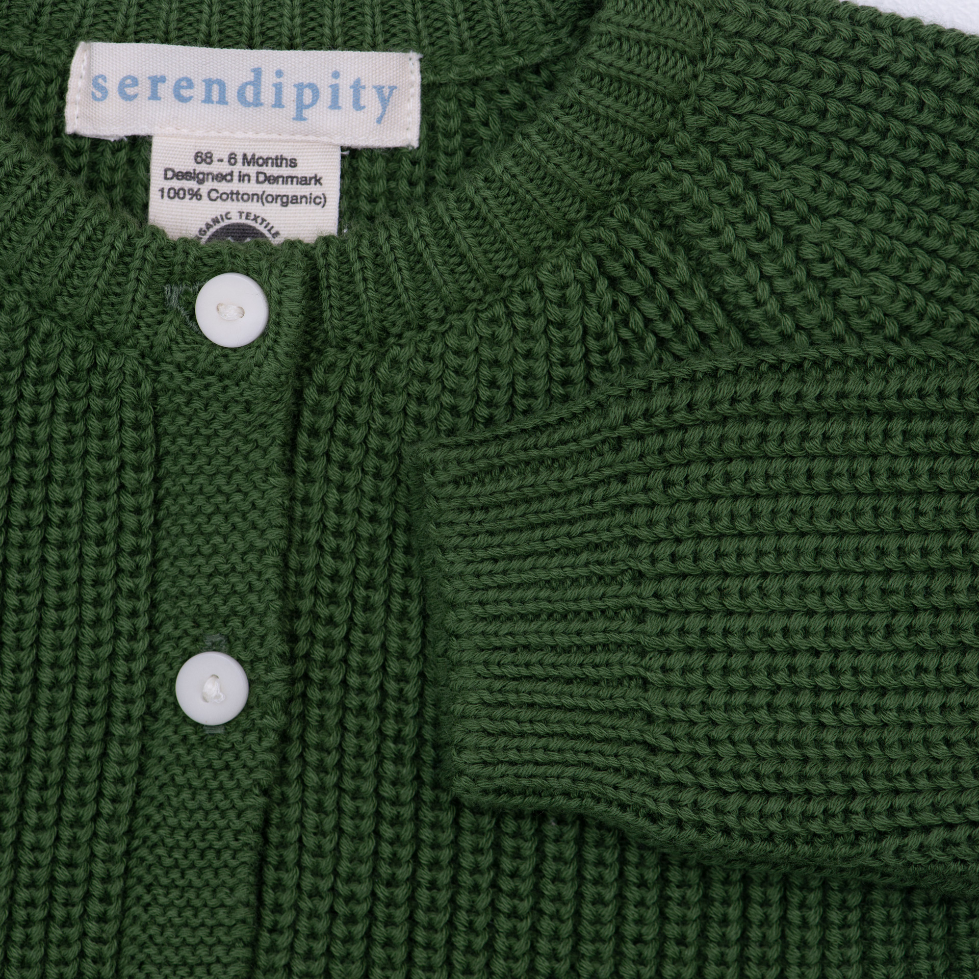 Close-up of a dark green knit cardigan sweater with white buttons and a visible 'serendipity' brand label.