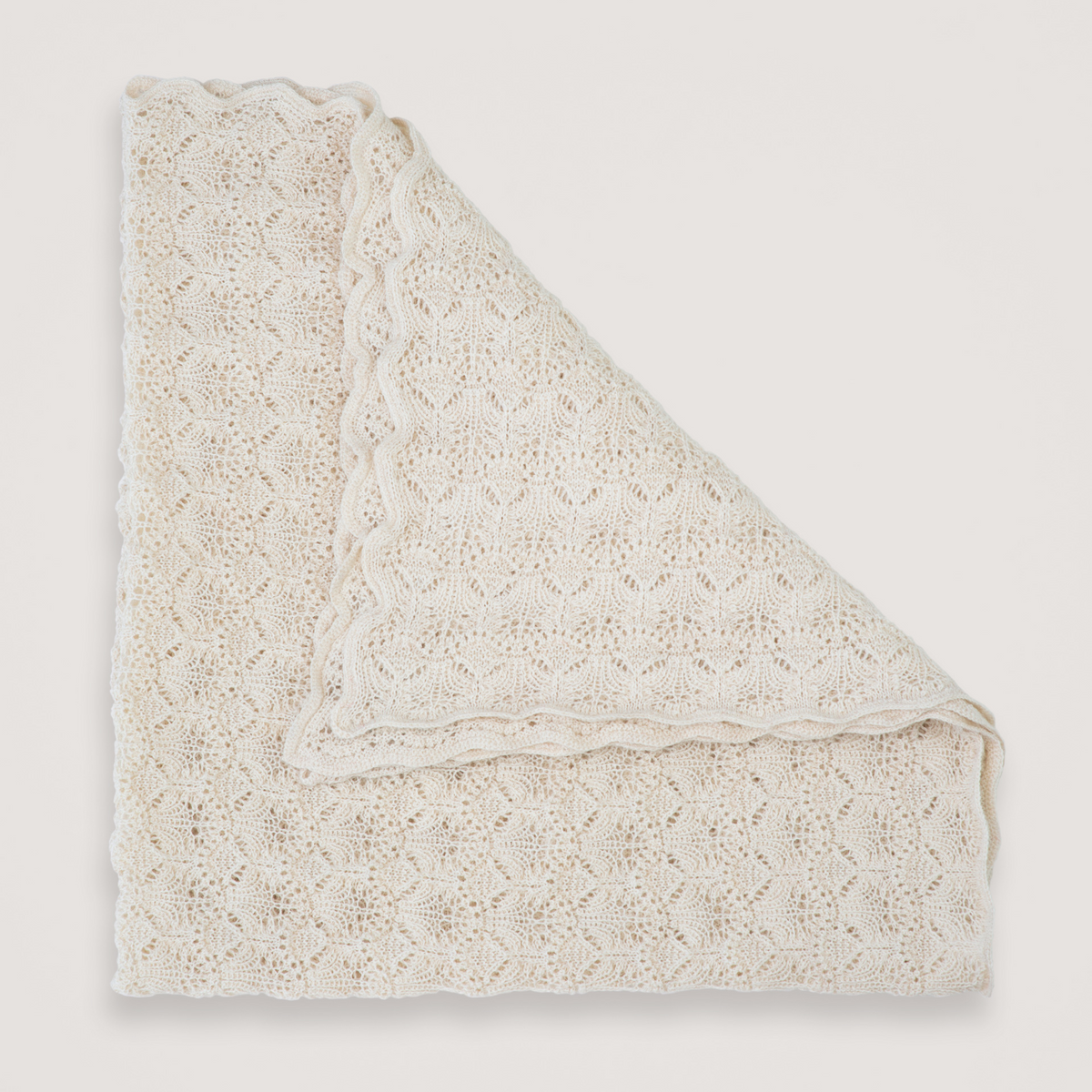An off-white knit lace blanket with a scalloped edge, folded neatly on a light beige background.