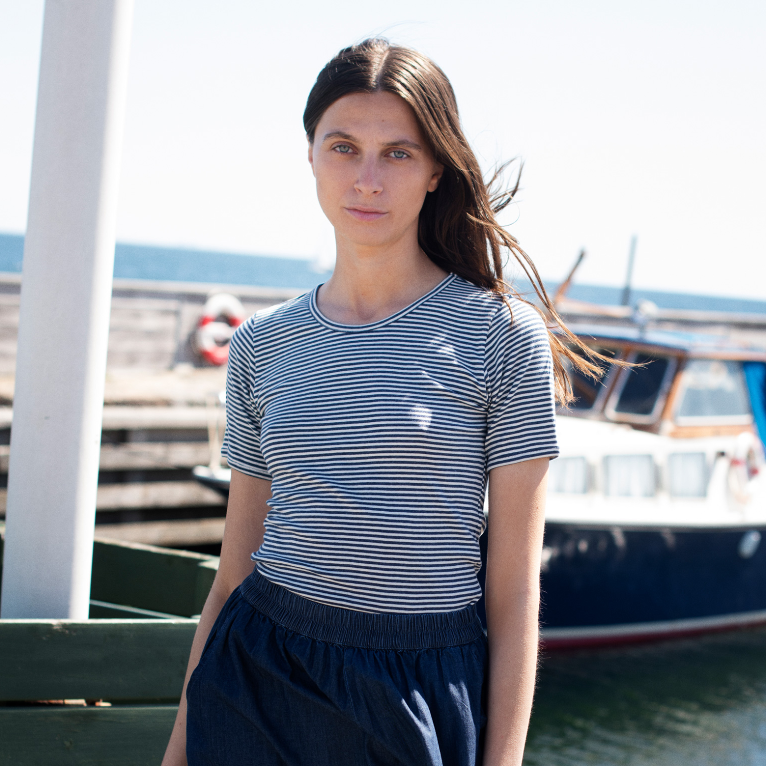 Woman wearing a striped shirt and dark pants by a marina with boats in the background