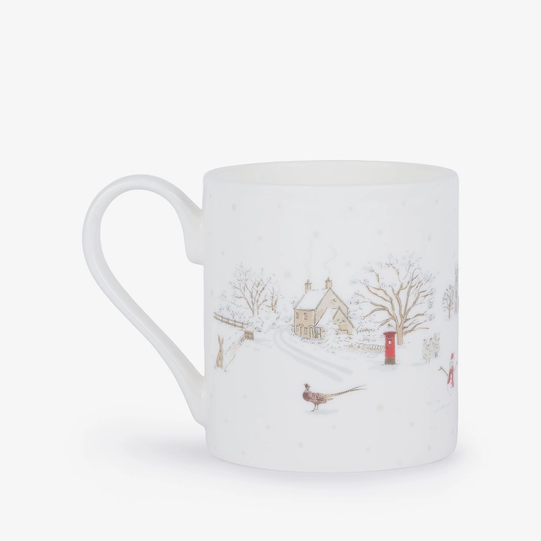 A white china mug featuring a delicate winter village illustration with snow-covered trees, a small house, a red post box, and a pheasant, set against a plain white background.