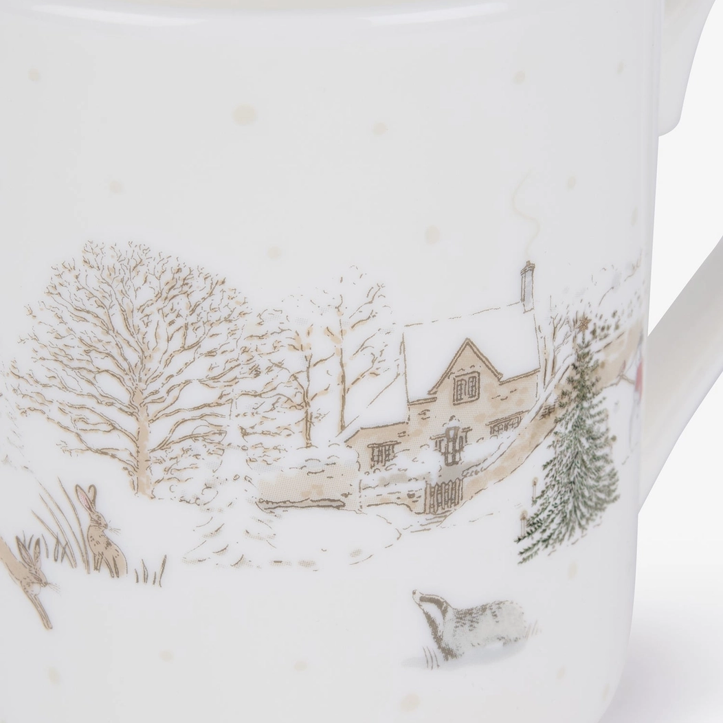 A close-up of a white china mug featuring a delicate winter landscape illustration with a cottage, bare trees, evergreen trees, and small animals in muted beige, gray, and green tones.