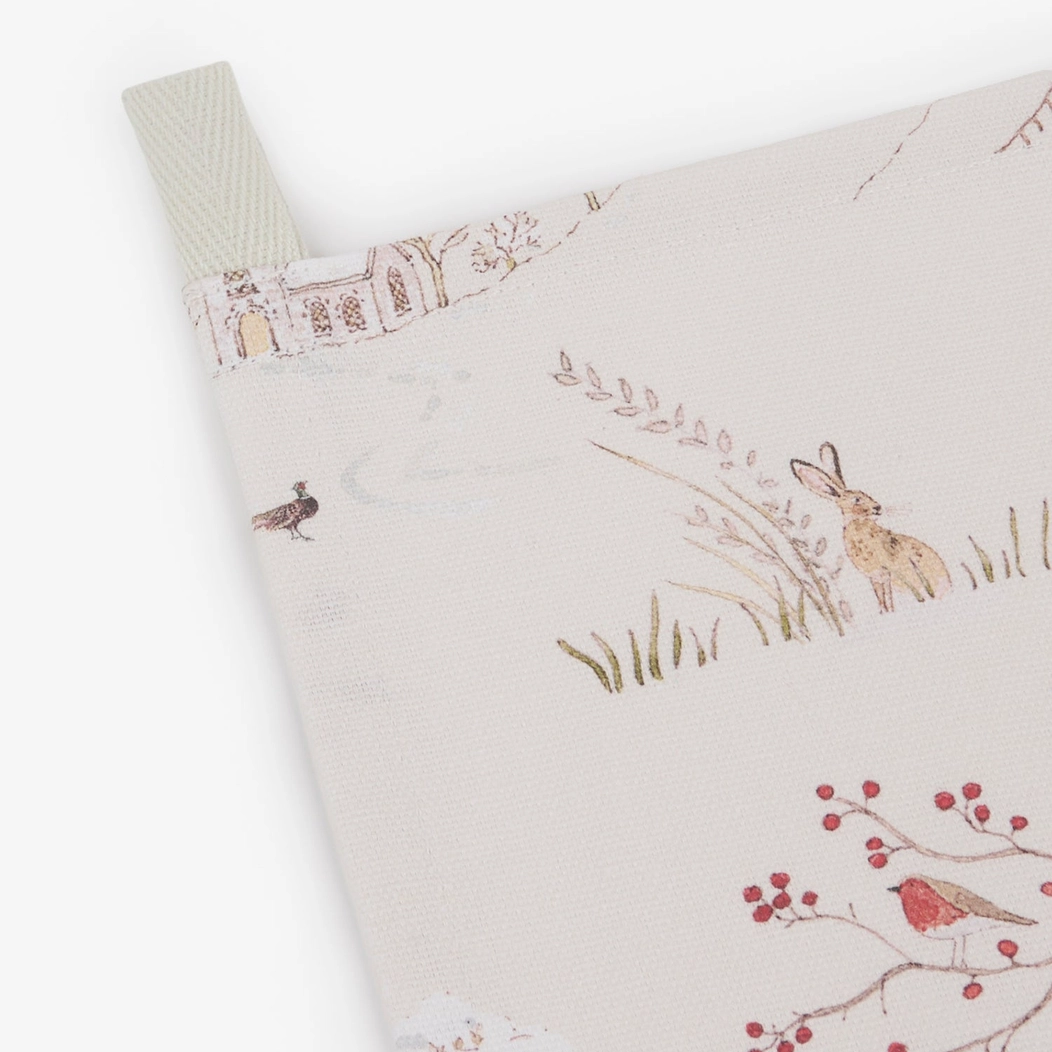 A close-up of a tea towel featuring a whimsical winter print with a rabbit, bird, red berries, and a small snowman.