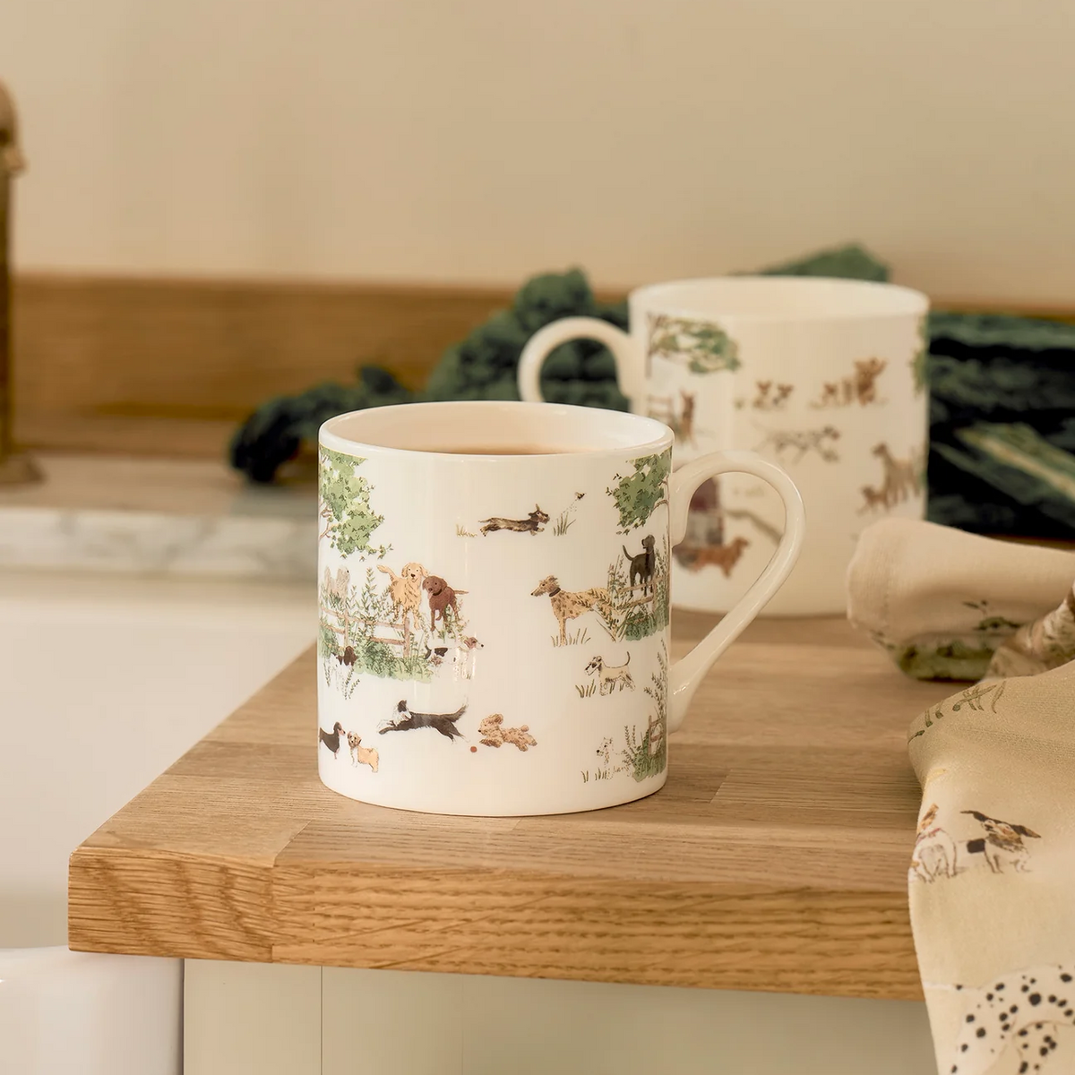 Two white ceramic mugs with detailed dog illustrations, displayed on a wooden kitchen counter with a neutral background.