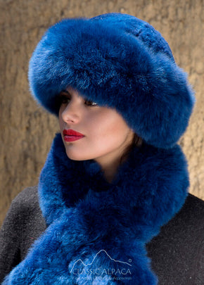 Premium Baby Alpaca Fur Hat. A woman wearing a blue alpaca fur hat and matching blue stole scarf in front of a natural background.