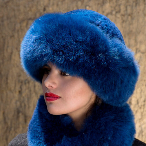 Premium Baby Alpaca Fur Hat. A woman wearing a blue alpaca fur hat and matching blue stole scarf in front of a natural background.
