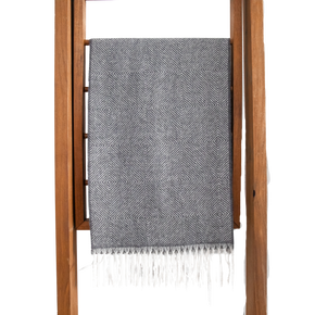 Gray patterned scarf with white fringe draped over a wooden ladder on a white background