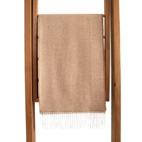 Beige woven scarf with white fringe draped over a wooden ladder on a white background