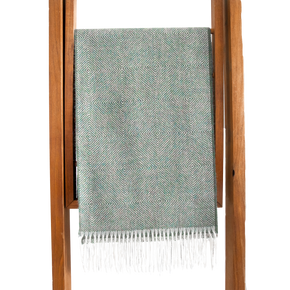 Teal woven blanket with white fringe on a wooden stand against a white background