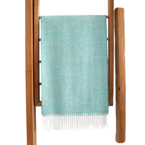 Teal woven blanket with white fringe draped over a wooden ladder