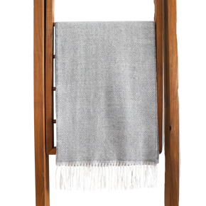 Gray woven blanket with white fringe draped over a wooden ladder on a white background