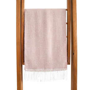 Pink woven blanket with white fringe on a wooden rack against a white background