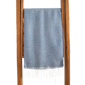 Blue patterned throw blanket with white fringe on a wooden ladder against a white background