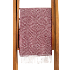 Pink woven blanket with white fringe draped over a wooden ladder on a white background