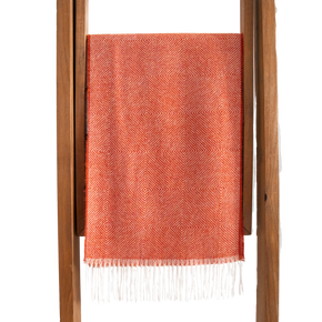 Coral woven blanket with white fringe on a wooden ladder against a white background