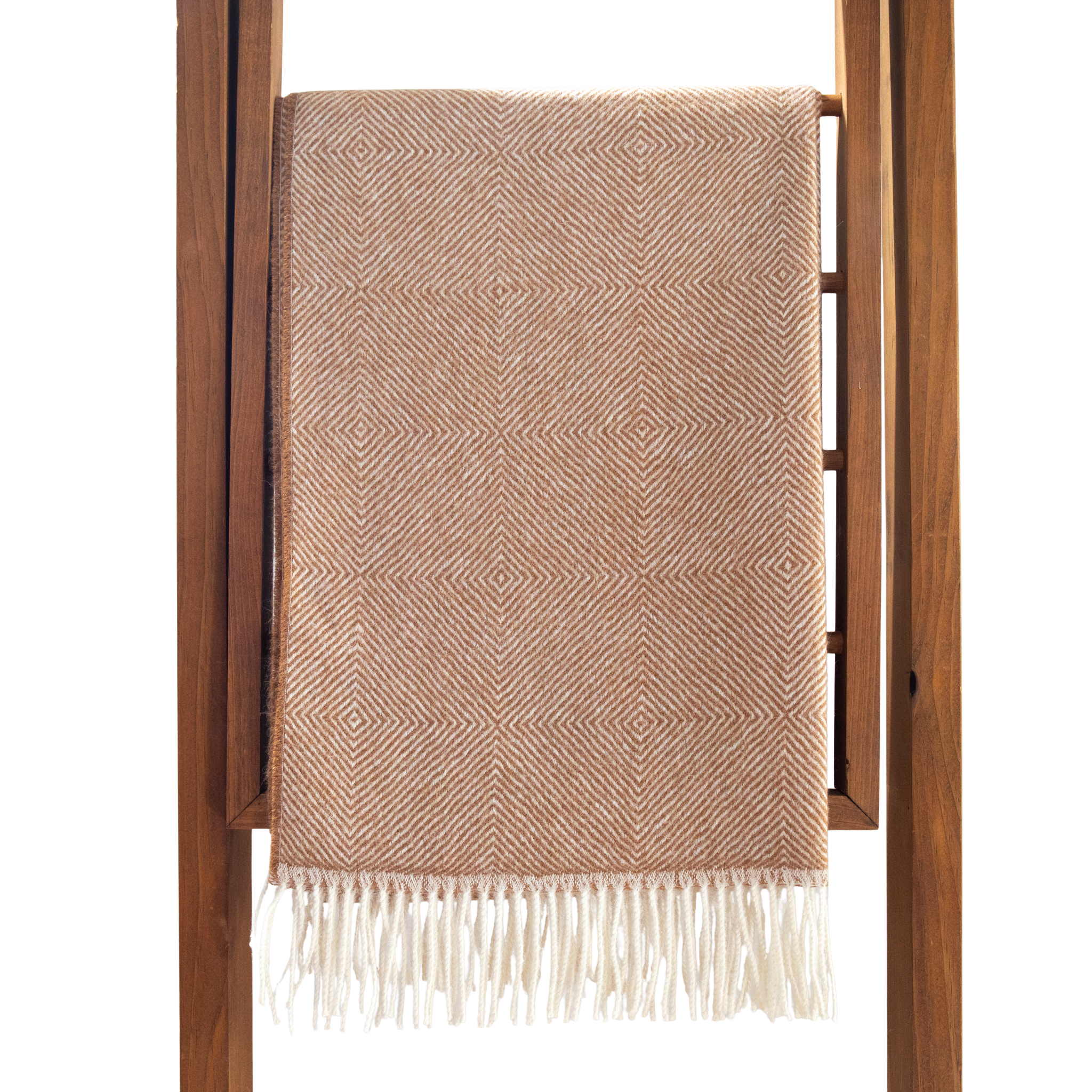 Fawn woven blanket with white fringe draped over a wooden ladder on a white background