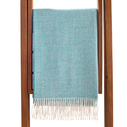 Teal blanket with white fringe draped over a wooden ladder on a white background
