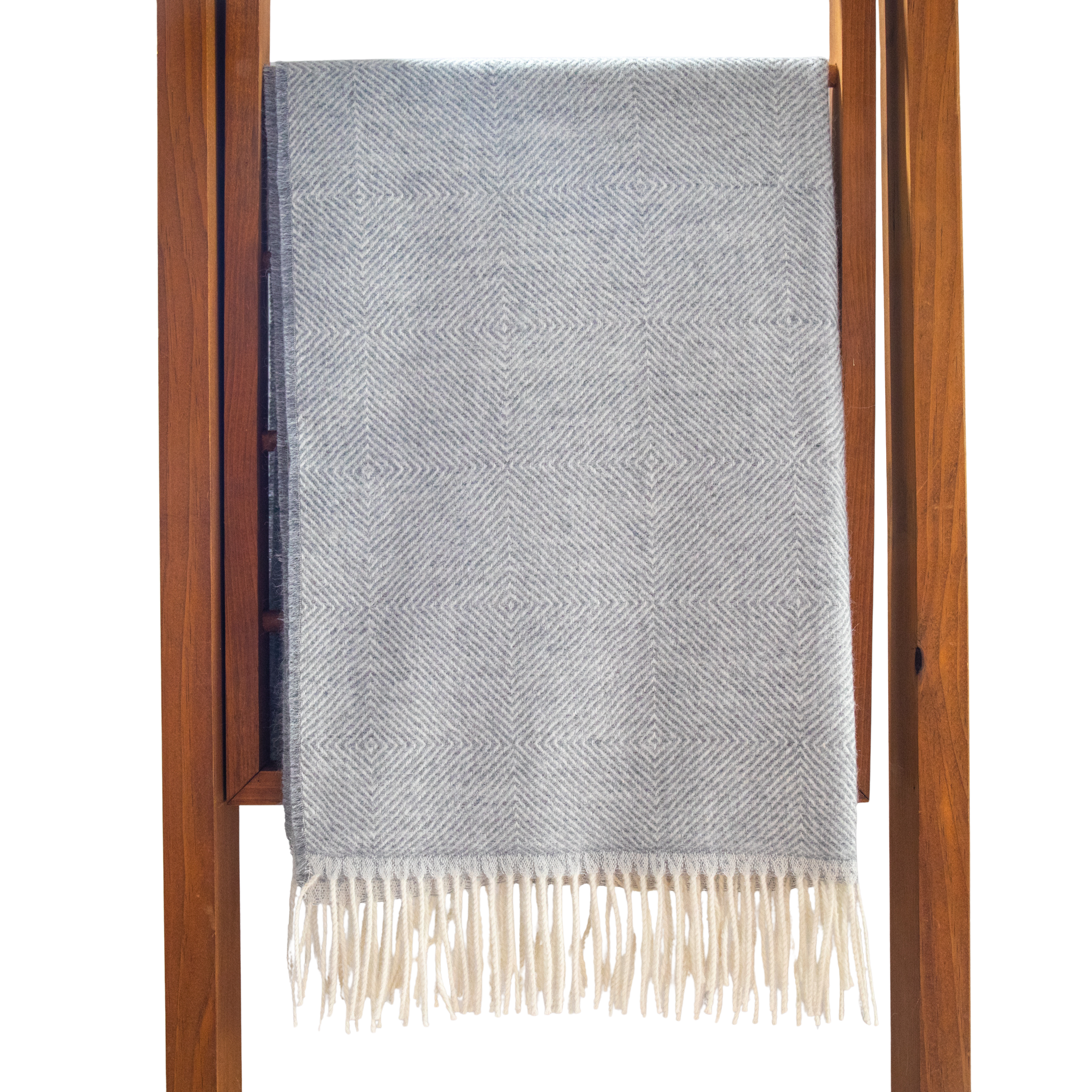 Light grey patterned throw blanket with white fringe draped over a wooden ladder on a white background