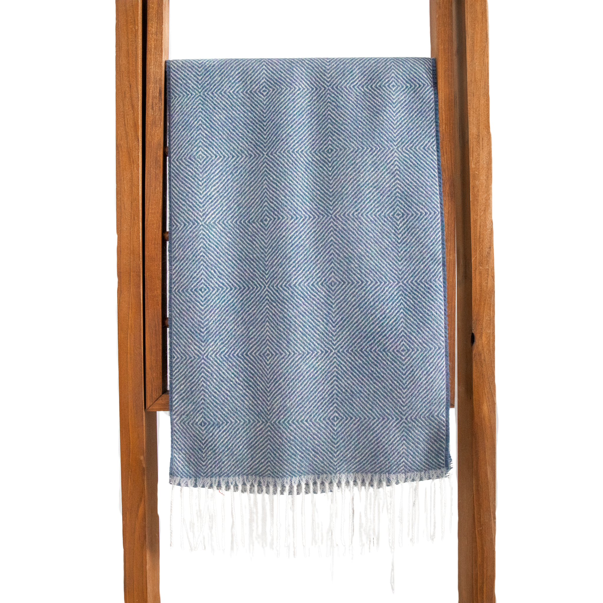 Blue patterned throw blanket with white fringe draped over a wooden ladder on a white background