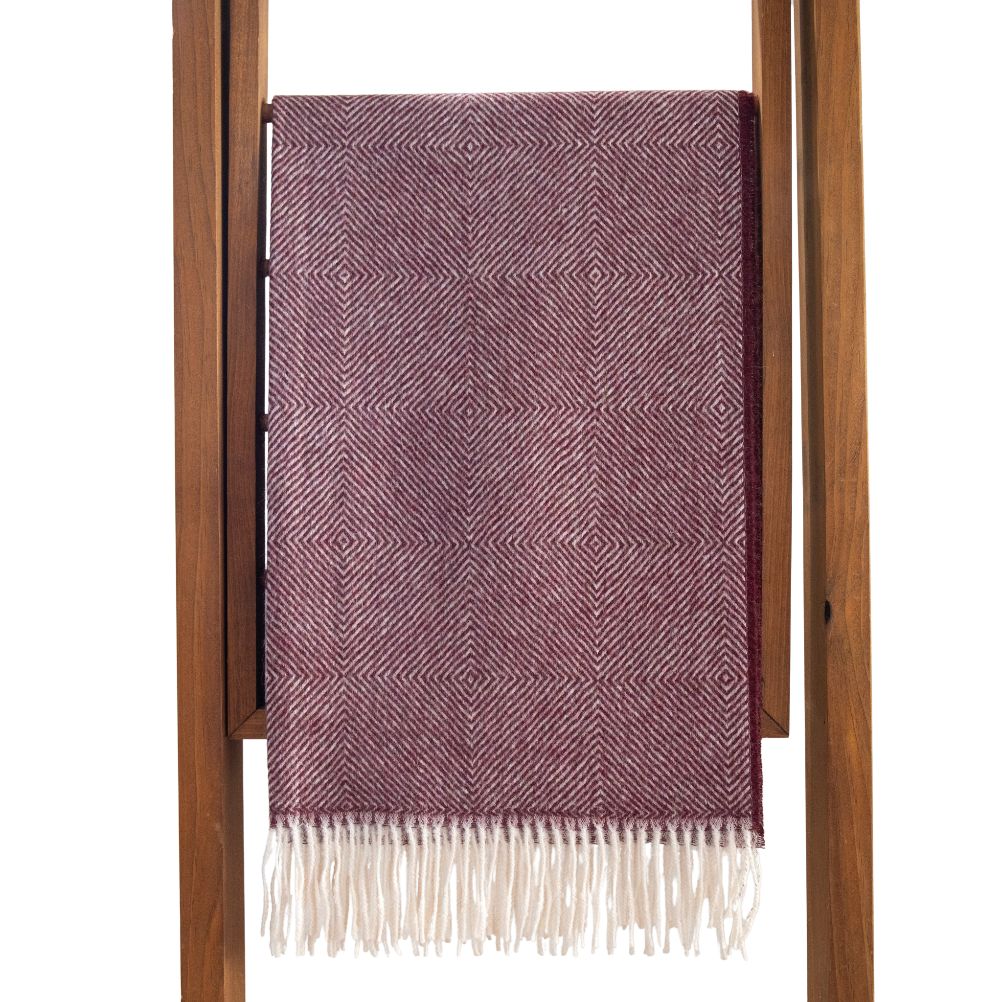 Purple patterned throw blanket with white fringe draped over a wooden rack on a white background