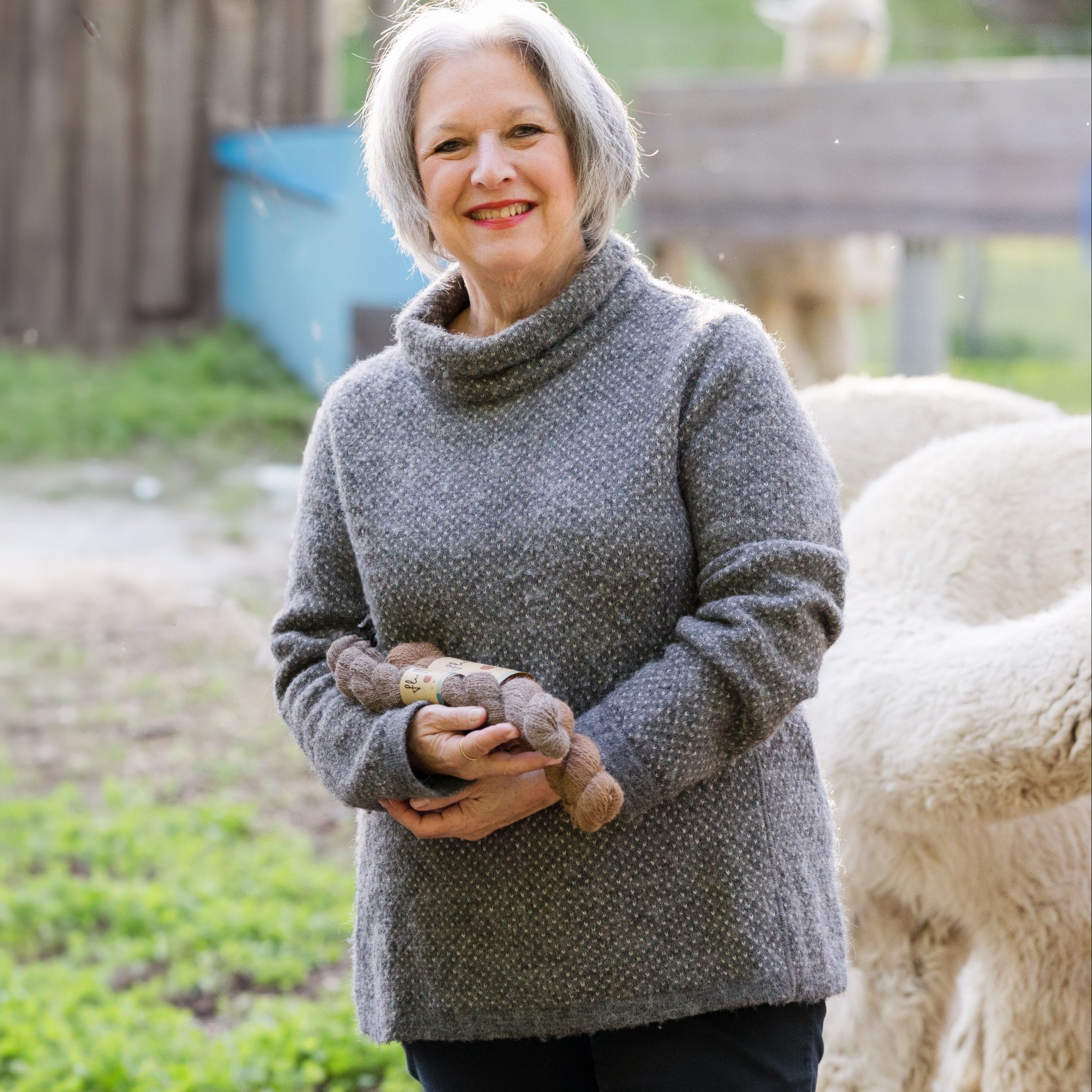 A woman standing outdoors wearing a gray mock turtleneck alpaca sweater.