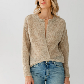 Woman wearing a beige sweater and blue jeans against a white background