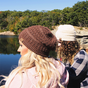 Person wearing a knit beanie sitting by a lake with trees in the background