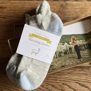 Gray sock with a label on a wooden surface, featuring an image of a person with alpacas.