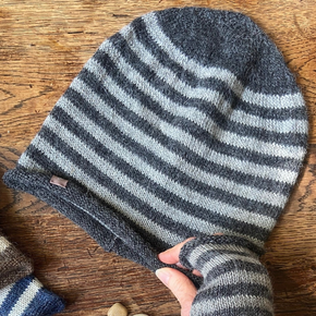 Striped knitted hat and mittens on a wooden surface with stones.