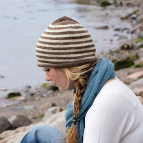 Person sitting by a body of water, reading a book, with a red bottle and backpack nearby.