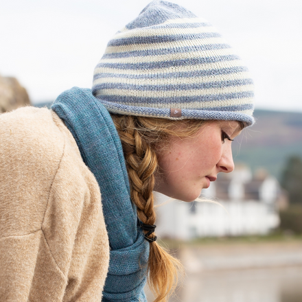 Person wearing a striped beanie and scarf by a lake with mountains in the background