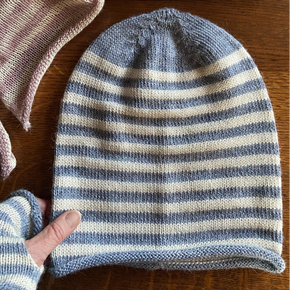 Two striped alpaca jersey knit beanies in pink and blue colors, displayed on a wooden surface.