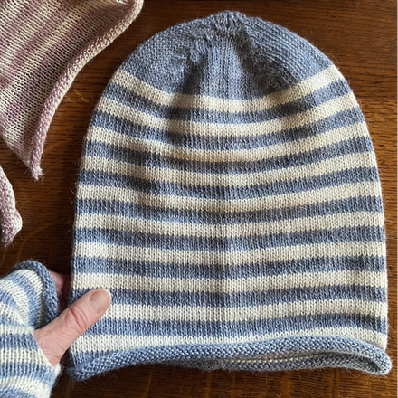 Two striped alpaca jersey knit beanies in pink and blue colors, displayed on a wooden surface.