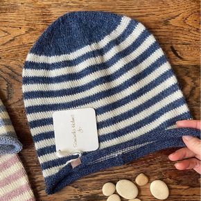 Blue and white striped knit beanie on a wooden surface with a hand holding it.