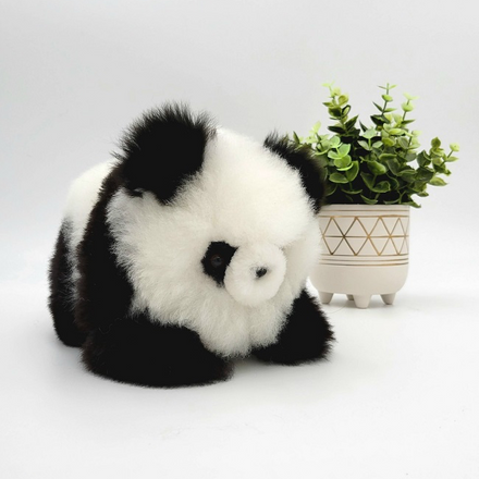 Plush alpaca fur panda standing next to a potted plant on a neutral background