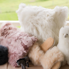 Collection of fluffy pillows and a plush toy on a surface with a blurred outdoor background
