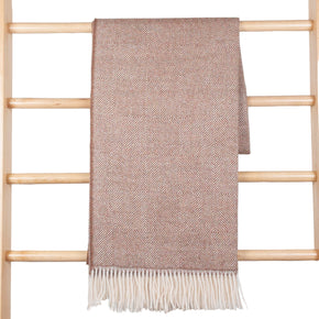Brown patterned throw blanket with white fringe draped over a wooden ladder against a white wooden panel background.