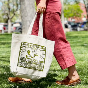 Person holding a white tote bag with green design in a park