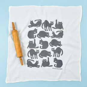 White towel with gray cat pattern and wooden rolling pin on a light blue background