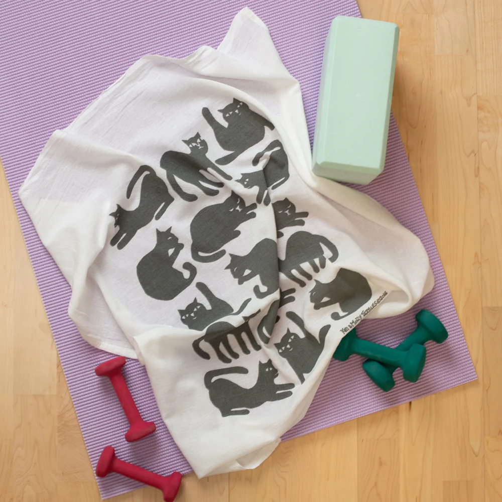 White towel with grey cat pattern on a purple mat with exercise equipment.