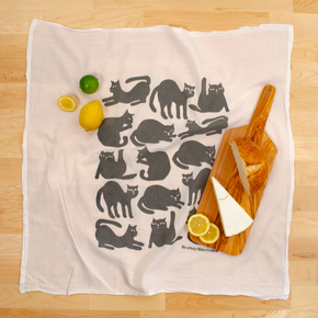 Kitchen towel with cat pattern on a wooden surface with lemons and a cutting board.