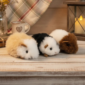 Three plush guinea pigs on a wooden surface with a plaid curtain and lantern in the background.