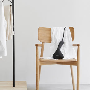 Cirrus No. 2 Steamer - black fabric steamer draped over white shirt and wooden chair on a neutral background