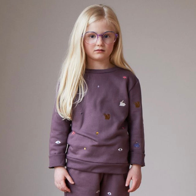 Oeuf Embroidered Sweatshirt -  a blonde child with glasses wears an embroidered purple sweatshirt in front of a neutral background. 
