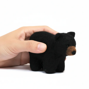 Hand holding a small black bear felted toy on a white background