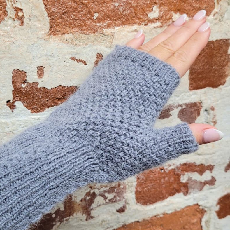 Gray knitted fingerless glove on a hand against a textured wall background