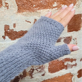 Gray knitted fingerless glove on a hand against a textured wall background