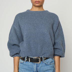 Person wearing a blue sweater and jeans against a plain background