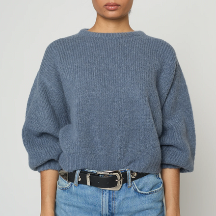 Person wearing a blue sweater and jeans against a plain background